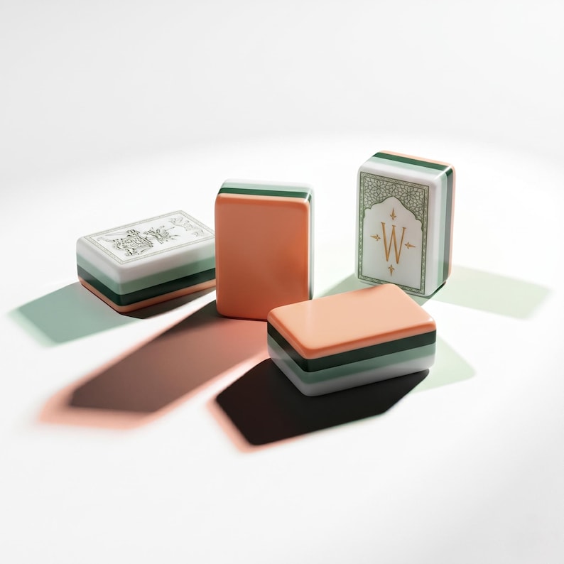 May include: Four rectangular mahjong tiles featuring a layered design of peach, dark green, and white. One tile displays a gold letter W inside a decorative frame, while another shows a detailed black and white illustration of a floral motif.