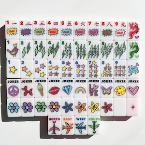 May include: A set of white rectangular mahjong tiles featuring colorful printed graphics including numbers, Chinese characters, lightning bolts, stars, flowers, hearts, rainbows, diamonds, lips, airplanes, and the word JOKER on specific tiles.
