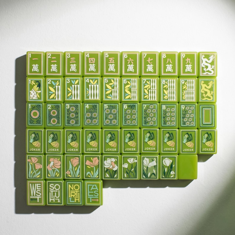 May include: A collection of rectangular mahjong tiles in shades of green, featuring various illustrations including Chinese characters, dragons, floral patterns, butterflies, and the words WEST, SOUTH, NORTH, and EAST printed on individual tiles.
