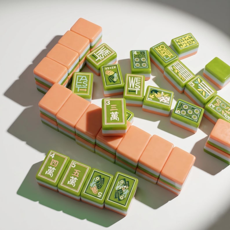 May include: A collection of rectangular mahjong tiles featuring a layered design with peach-colored tops and green and white bases. The tiles display various green engraved symbols, Chinese characters, and directional markers like West and East.