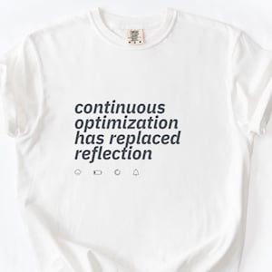 May include: A white short-sleeved t-shirt featuring the dark gray text "continuous optimization has replaced reflection" printed on the chest. Below the text are four small icons representing a cloud, a battery, a loading circle, and a bell.