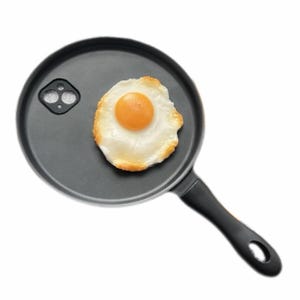 May include: A round black non-stick frying pan with a long handle featuring a hole for hanging. Inside the pan, there is a single fried egg with a bright yellow yolk and a cooked white, alongside a small black square-shaped camera lens protector.