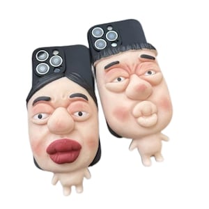 May include: Two black smartphone cases featuring three-dimensional, sculpted faces with exaggerated features. One face has dark hair, a large nose, and prominent red lips. The other face has dark hair, a large nose, and puckered lips.