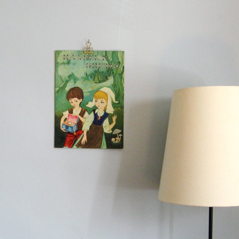 May include: Vintage children's book cover featuring two children, a boy and a girl, in a woodland setting. The book title is "Hansel & Gretel".