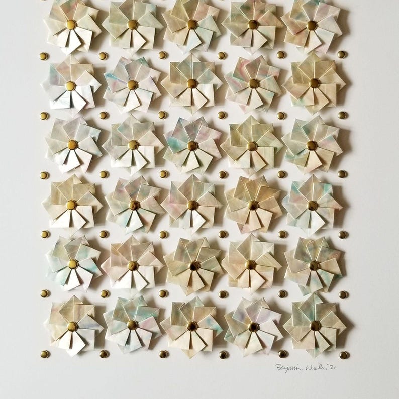 A close up of the bottom portion of the artwork showing small origami flowers mounted on a white background with gold metal pins. The flowers are arranged in a grid pattern. The artwork is signed in the bottom right corner.