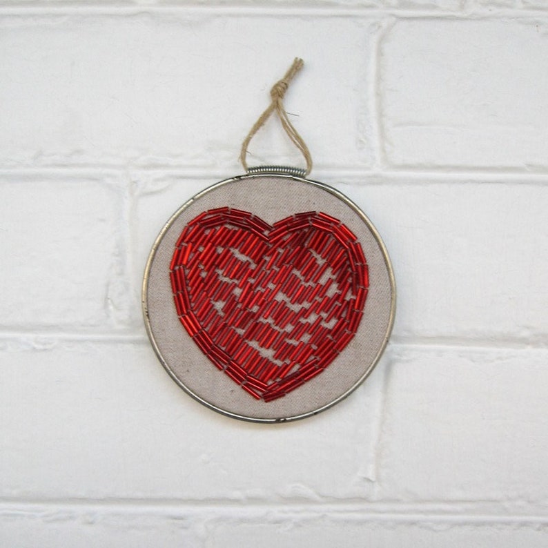 May include: A red beaded heart embroidered on a beige fabric in a round embroidery hoop.