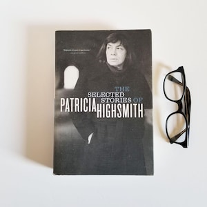 May include: A black and white photo of Patricia Highsmith on the cover of a book titled "The Selected Stories of Patricia Highsmith".