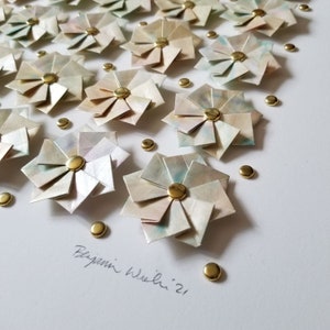A close up of the bottom right portion of the artwork showing small origami flowers mounted on a white background with gold metal pins. The artwork is signed in pencil.