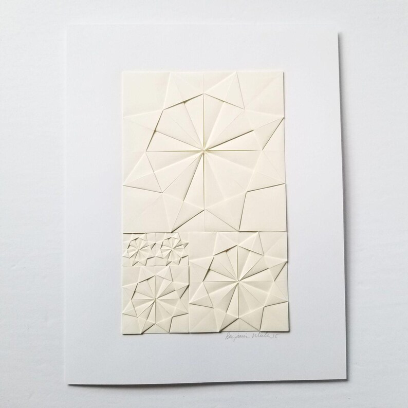 an origami artwork of ivory coloured paper on a white background. The artwork is a geometric design made of folded paper squares. The design is made up of several different shapes, including circles, squares, and triangles. The design is symmetrical and has a radial pattern. The artwork is signed in the bottom right corner.