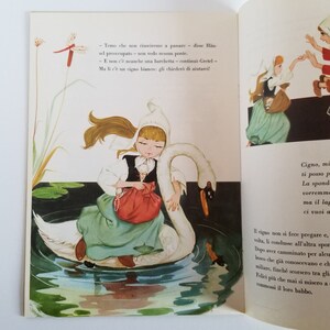 May include: A young girl in a white dress and a red bag sits on a white swan. The swan is swimming in a blue pond with green lily pads. The girl has blonde hair and blue eyes. The text in the image reads: "Temo che non riusciremo a passare - disse H&auml;nsel preoccupato - non vedo nessun ponte. - E non c'&egrave; neanche una barchetta - continuo Gretel - Ma li c'&egrave; un cigno bianco: gli chieder&ograve; di aiutarci!"