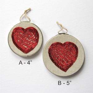 May include: Two embroidered heart-shaped wall hangings with red beading. The smaller one is 4 inches in diameter and the larger one is 5 inches in diameter.