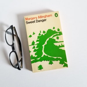 May include: A paperback book with a white cover and green and black illustrations. The title of the book is "Sweet Danger" by Margery Allingham.