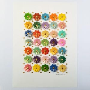 A white background with a grid of 36 colorful origami flowers with gold accents. The signature is in the bottom right corner.