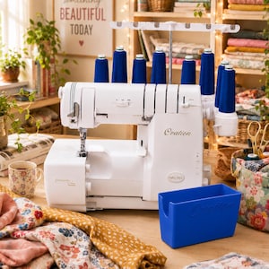 Könnte beinhalten: Eine weiße Baby Lock Ovation Overlock-Nähmaschine mit acht blauen Garnrollen auf einem oberen Halter. Die Maschine trägt die Aufschrift Ovation und ExtraordinAir und wird von einem passenden blauen Kunststoff-Abfallbehälter ergänzt.