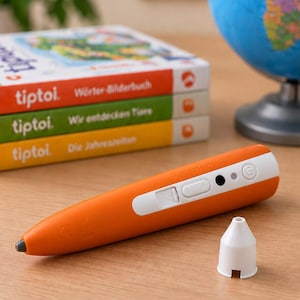 Pode incluir: Uma caneta de aprendizagem interativa laranja e branca com uma pequena ponta preta, um botão de energia branco, controlos de volume e uma porta USB. Uma tampa cónica branca separada está ao lado da caneta numa superfície de madeira.