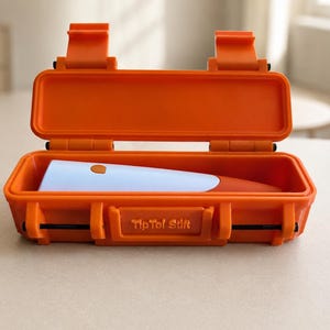 Könnte beinhalten: Ein leuchtend orangefarbener, rechteckiger Hartschalenkoffer mit zwei Verschlüssen und einem Klappdeckel, der geöffnet ein hellblaues und orangefarbenes Handgerät im Inneren zeigt. Auf der Vorderseite des Koffers ist der Text TipToi Stift eingeprägt.