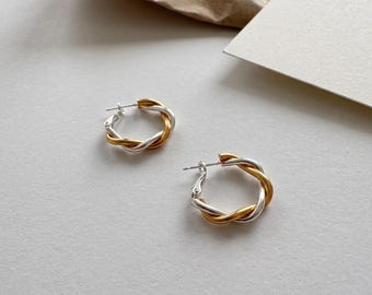 May include: A pair of hoop earrings featuring a twisted design with alternating strands of polished silver-tone and gold-tone metal. Each earring has a secure post-back closure and a circular shape formed by the intertwined metallic wires.