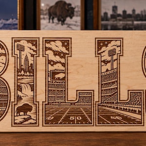 Peut inclure: Une plaque rectangulaire en bois clair gravée au laser avec le mot BILLS en grandes lettres capitales. Chaque lettre contient des illustrations détaillées d'un stade de football, d'une ville, d'une cascade, d'un bison et de supporters.