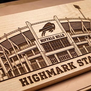Puede incluir: Una placa rectangular de madera clara con una ilustración detallada grabada con láser del estadio Highmark Stadium. El diseño incluye el logotipo de los Buffalo Bills, el texto Buffalo Bills y el texto Highmark Stadium en letras negritas.