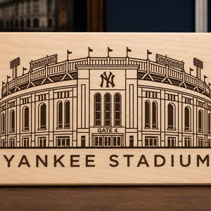 Może przedstawiać: Prostokątna tabliczka z jasnego drewna z ciemnobrązową, grawerowaną laserowo ilustracją Yankee Stadium. Wzór przedstawia fasadę stadionu, logo NY oraz wyśrodkowany u dołu napis GATE 4 i YANKEE STADIUM.