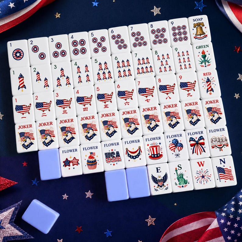 Puede incluir: Un juego de fichas de Mahjong blancas con dise&ntilde;os patri&oacute;ticos rojos, blancos y azules. Las fichas presentan estrellas, fuegos artificiales, la bandera estadounidense y la Estatua de la Libertad. Incluye estantes de fichas azules.
