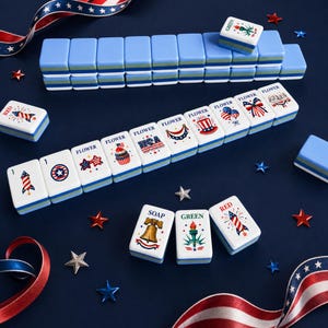 Puede incluir: Un juego de fichas de Mahjong azules y blancas con dise&ntilde;os patri&oacute;ticos rojos, blancos y azules. Las fichas est&aacute;n dispuestas sobre una superficie azul oscuro con decoraciones en forma de estrella y cinta roja, blanca y azul.