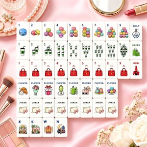 Op de afbeelding: Een set witte Mahjong-tegels met kleurrijke illustraties van macarons, koffiekopjes, handtassen en bloemen. De tegels bevatten ook cijfers, Chinese karakters en de woorden "SOAP", "GREEN" en "RED".