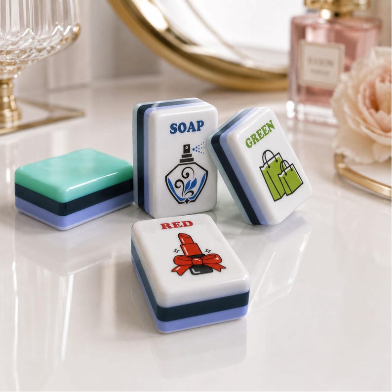 Op de afbeelding: Een verzameling decoratieve zeepbakjes met een rechthoekige vorm. E&eacute;n is lichtgroen en de andere zijn wit met blauwe en zwarte randen. De witte bakjes hebben illustraties van een parfumfles, boodschappentassen en lippenstift, met de woorden "SOAP", "GREEN" en "RED".