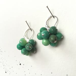 Puede incluir: Un par de pendientes de plata con racimos de piedras preciosas verdes. Cada pendiente presenta un racimo de peque&ntilde;as piedras preciosas verdes redondas.