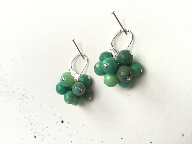 Puede incluir: Un par de pendientes de plata con racimos de piedras preciosas verdes. Cada pendiente presenta un racimo de peque&ntilde;as piedras preciosas verdes redondas.