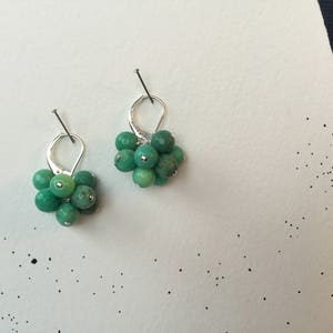 Puede incluir: Un par de pendientes de plata con racimos de piedras preciosas verdes. Cada pendiente presenta un racimo de peque&ntilde;as piedras preciosas verdes redondas.