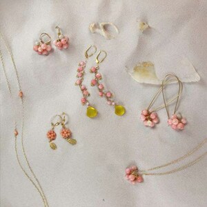 Puede incluir: Un conjunto de pendientes y collares de cuentas rosas y amarillas. Los pendientes est&aacute;n hechos con peque&ntilde;as cuentas rosas y tienen una cuenta amarilla colgante. Los collares est&aacute;n hechos con peque&ntilde;as cuentas rosas y tienen una cadena delicada.