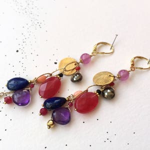 Puede incluir: Un par de pendientes de oro con un racimo de piedras preciosas de colores. Los pendientes presentan piedras rosas, rojas, moradas y azules, así como detalles dorados.