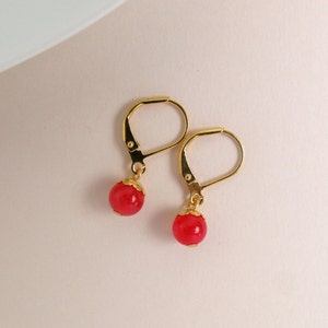 Puede incluir: Un par de pendientes de oro con gotas de piedras preciosas rojas. Los pendientes tienen un diseño simple y elegante.