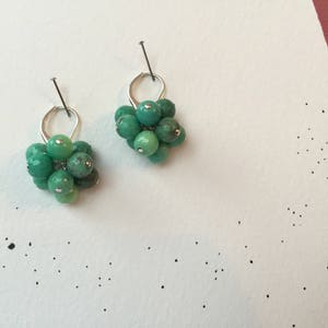 Puede incluir: Un par de pendientes de plata con racimos de piedras preciosas verdes. Cada pendiente presenta un racimo de peque&ntilde;as piedras preciosas verdes redondas.