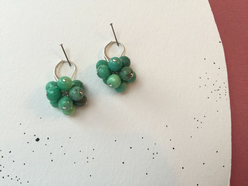 Puede incluir: Un par de pendientes de plata con racimos de piedras preciosas verdes. Cada pendiente presenta un racimo de peque&ntilde;as piedras preciosas verdes redondas.