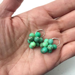 Puede incluir: Un par de pendientes de aro de plata con cuentas de piedras preciosas verdes. Las cuentas est&aacute;n agrupadas en forma de flor.