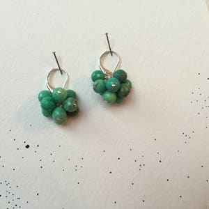 Puede incluir: Un par de pendientes de plata con cuentas de piedras preciosas verdes. Los pendientes tienen la forma de un racimo de peque&ntilde;as cuentas redondas.