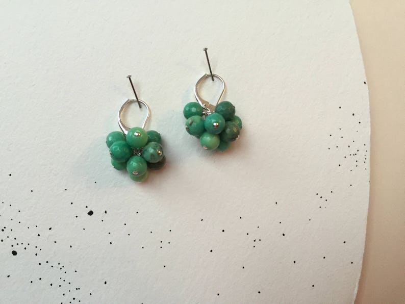 Puede incluir: Un par de pendientes de plata con cuentas de piedras preciosas verdes. Los pendientes tienen la forma de un racimo de peque&ntilde;as cuentas redondas.