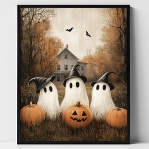 May include: A framed Halloween-themed print featuring three white ghosts wearing black witch hats, standing in front of a house and pumpkins. Two bats fly in the sky above the house. The pumpkins are orange and the background is a fall landscape.