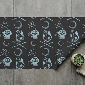 May include: A rectangular sheet of dark gray wrapping paper featuring a repeating pattern of light blue illustrations. The design includes small skulls with crossed bones, crescent moons, and hooded figures holding scythes in a consistent layout.