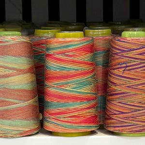 May include: A collection of cylindrical spools of thread arranged in rows. Each spool features a distinct variegated colour pattern, including combinations of orange, green, red, yellow, purple, and brown, with light green plastic caps on top.