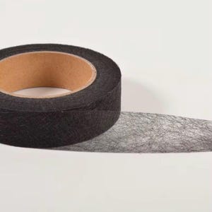 May include: A roll of black fibrous tape with a textured, semi-transparent appearance. The tape is wound around a light brown cardboard core, showing a distinct cross-hatched pattern of thin, dark fibres throughout the material surface.