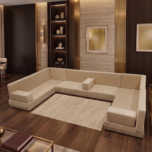 May include: A large, U-shaped modular sectional sofa upholstered in a light beige, ribbed fabric. The sofa features a low-profile design with integrated backrests and armrests, arranged to create a spacious seating area around a central rug.