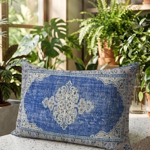 Könnte beinhalten: Ein rechteckiges Zierkissen mit einem leuchtend blauen und cremeweißen, komplexen Medaillonmuster. Das Design ahmt einen traditionellen Teppich nach, mit einem zentralen verzierten Motiv, einer dekorativen Bordüre und einer abgenutzten Textur.