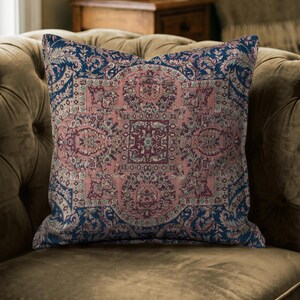 May include: A square throw cushion featuring a detailed, intricate pattern in shades of dusty pink, deep navy blue, and cream. The design displays a central medallion surrounded by ornate floral and geometric motifs, mimicking the style of a rug.