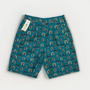 May include: Teal-colored shorts with an all-over pattern of gold and navy crests. The shorts have a pleated front and a tag that reads "Polo Club". The shorts are a casual style.