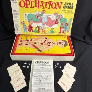 Może przedstawiać: Gra zręcznościowa "Operation" w stylu vintage w oryginalnym pudełku. Żółte pudełko zawiera ilustracje lekarzy i pacjenta. Plansza do gry przedstawia pacjenta z różnymi dolegliwościami. Zawiera karty do gry i instrukcje.