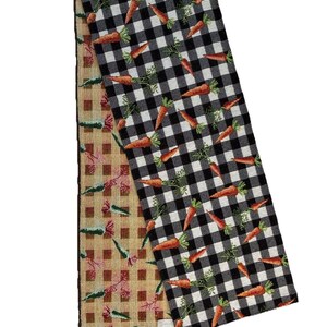 May include: A rectangular table runner featuring a dual-sided design. One side displays a black and white buffalo check pattern with orange carrots and green tops. The reverse side features a tan and brown checkered pattern with carrots.
