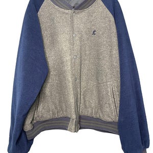 Puede incluir: Una chaqueta estilo universitario con cuerpo de forro polar gris jaspeado y mangas de forro polar azul sólido. La chaqueta tiene cuello y puños acanalados con rayas grises, cierre frontal con botones a presión y un pequeño icono de Mickey bordado.